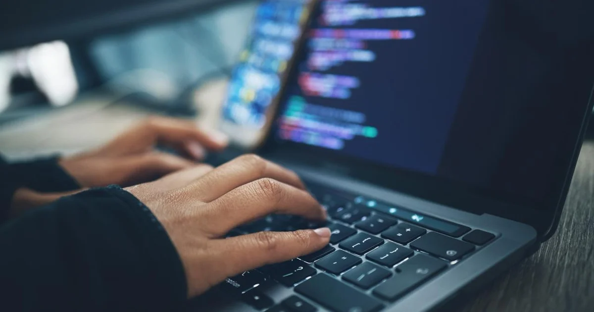 Developer typing on laptop with code on screen