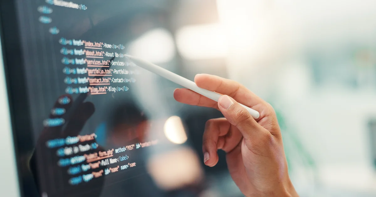 Mano con un lápiz digital señalando líneas de código HTML en una pantalla, revisando el código a mano