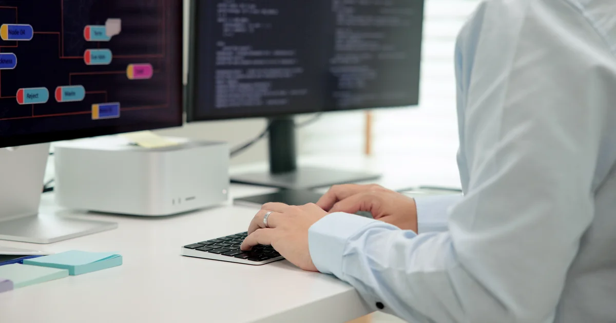 Un programador escribe en su mesa con código y un diagrama de flujo en dos pantallas, el trabajo de quien mantiene proyectos de código abierto y corrige sus fallos