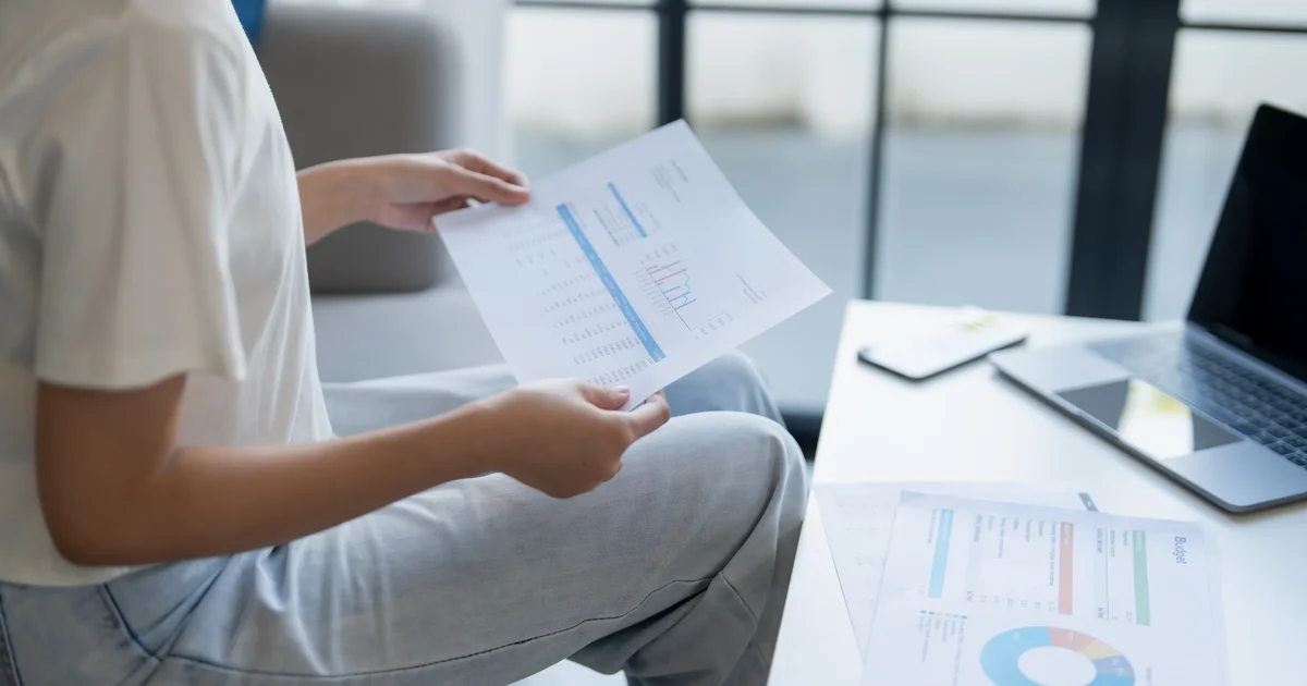 Una persona revisa informes impresos junto a un portátil, documentos que en Europa podrán llevar la marca invisible de ChatGPT si se escribieron con él