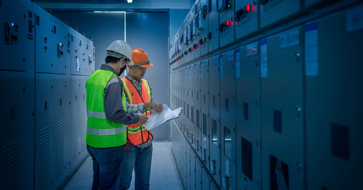 Dos ingenieros con casco revisan planos entre filas de armarios eléctricos, mientras los operadores de centros de datos mantienen en secreto su consumo de agua y luz