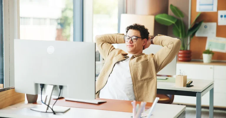 Empleado relajado con las manos detrás de la cabeza frente al ordenador, como si un agente de IA como Muse Wonder de Meta trabajara por él