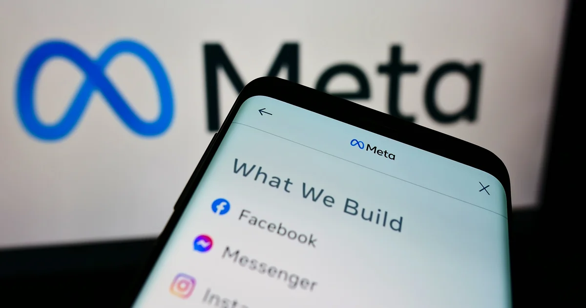 Móvil con la página What We Build de Meta, con Facebook, Messenger e Instagram, delante de un gran logotipo de Meta