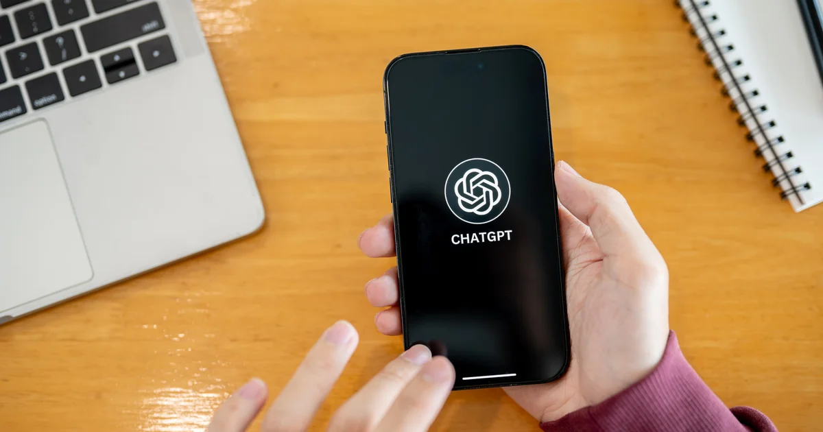 Una mano sostiene un móvil con el logotipo de ChatGPT junto a un portátil, el producto de OpenAI detrás de las cifras que hundieron a las tecnológicas