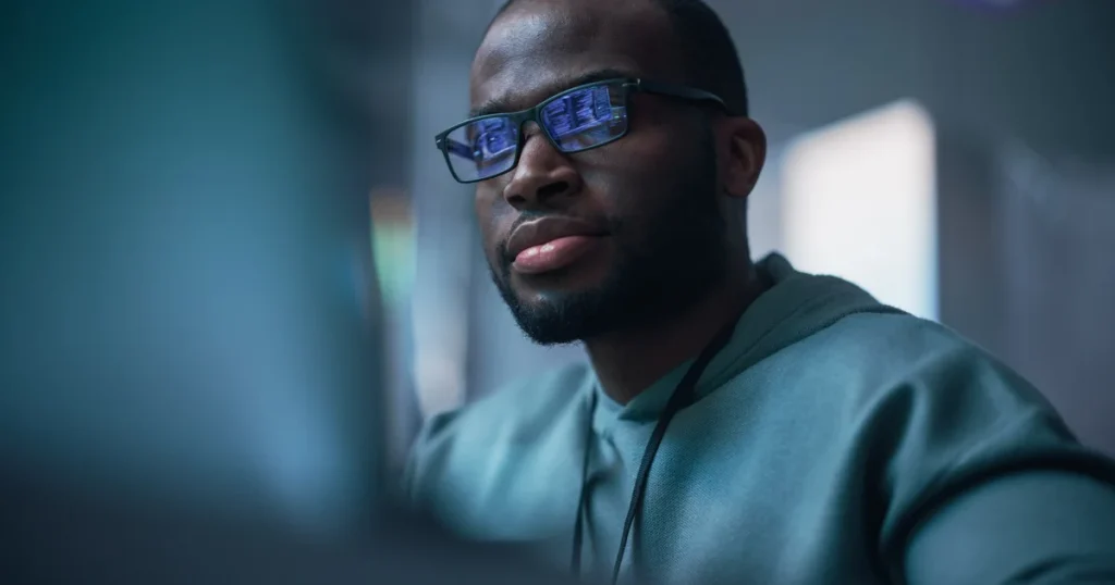 Programador con gafas frente a la pantalla del ordenador, con el código reflejado en los cristales, para ilustrar a las empresas que usan la API de OpenAI y pagan un 10% más por tener los datos en Europa