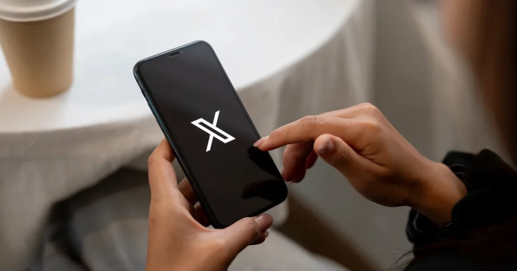Una persona sujeta un móvil con el logo de X, la marca de la nueva suscripción que junta Grok, Cursor y X Premium